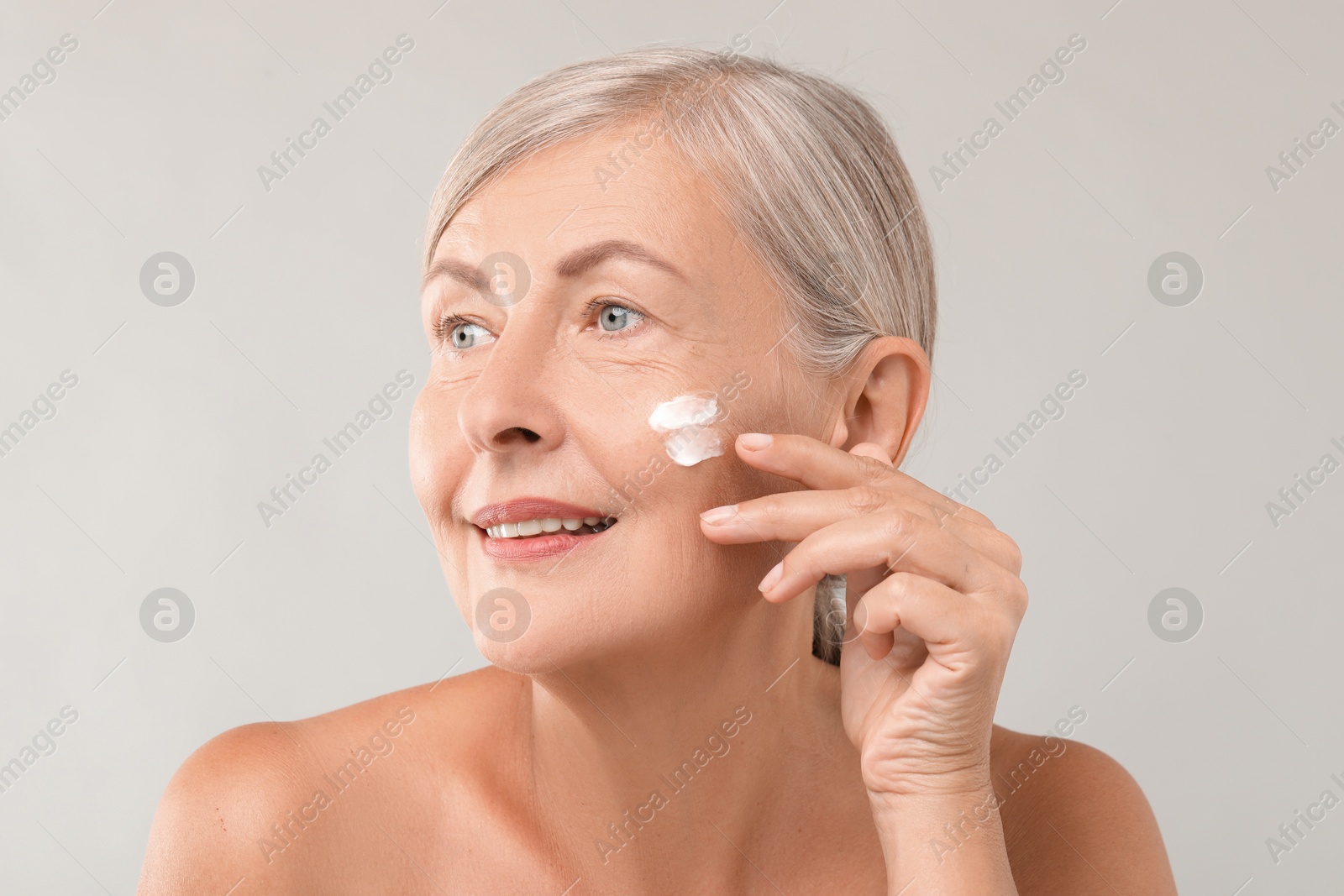 Photo of Senior woman with face cream on light background