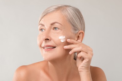 Senior woman with face cream on light background