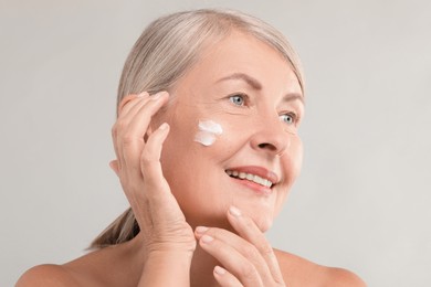 Senior woman with face cream on light background