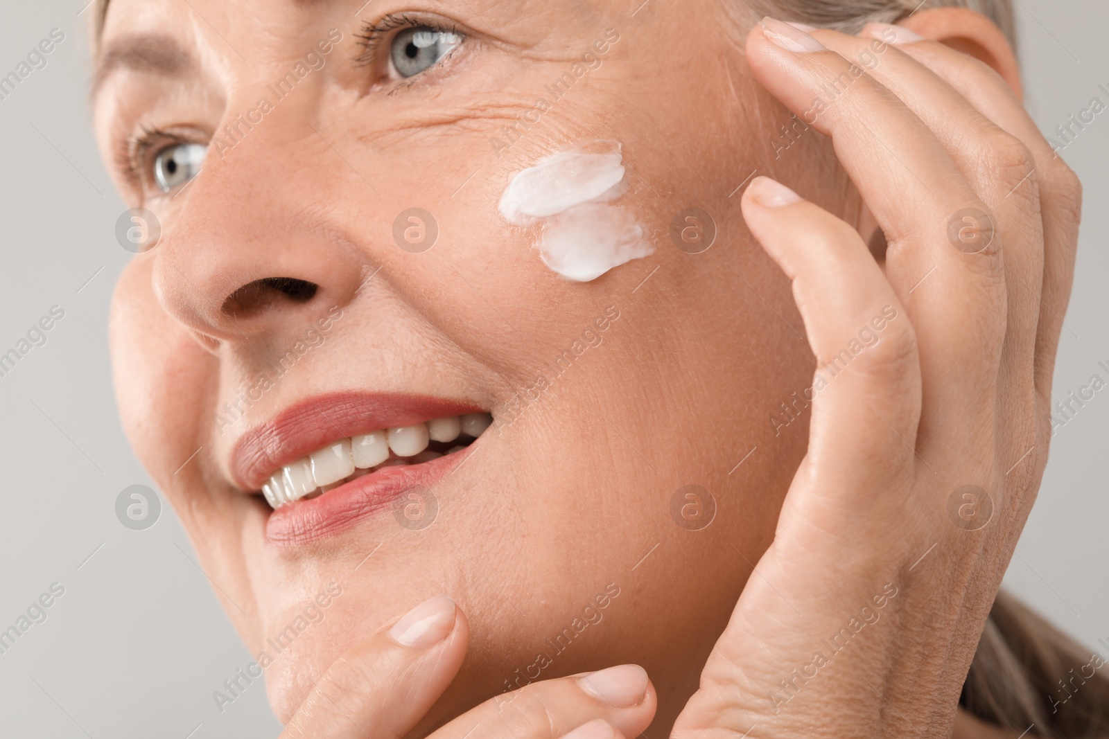 Photo of Senior woman with face cream on light background, closeup