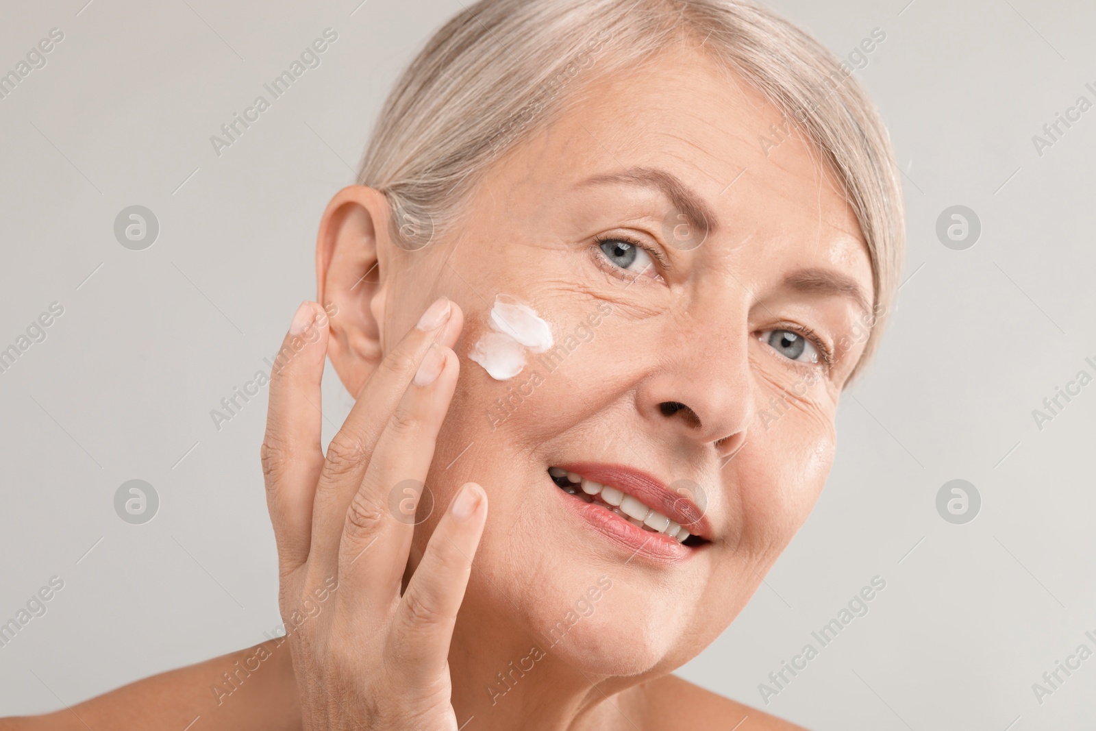 Photo of Senior woman applying face cream on light background, closeup