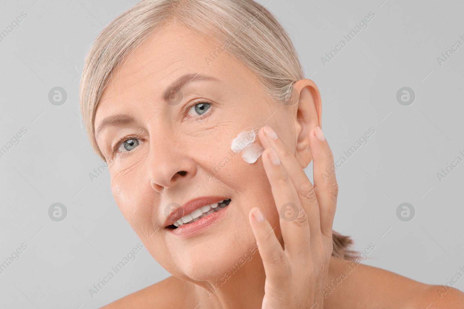 Photo of Senior woman applying face cream on light background, closeup