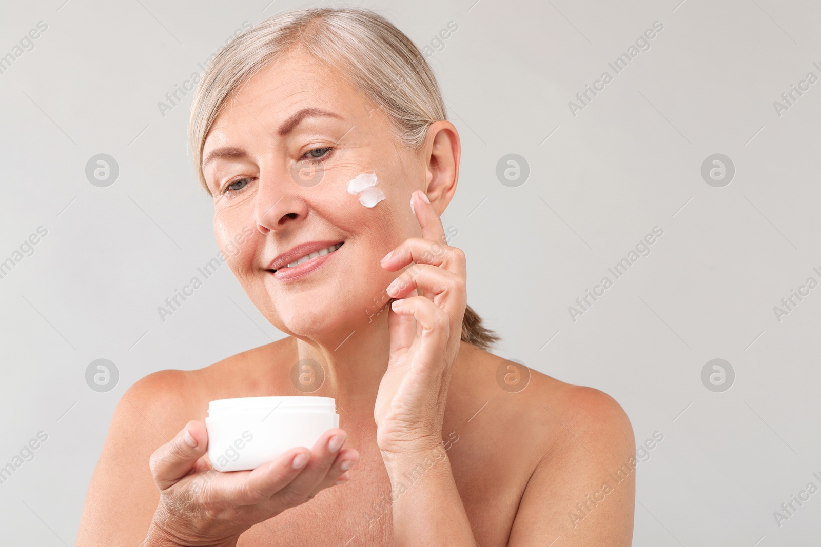 Photo of Senior woman applying face cream on light background