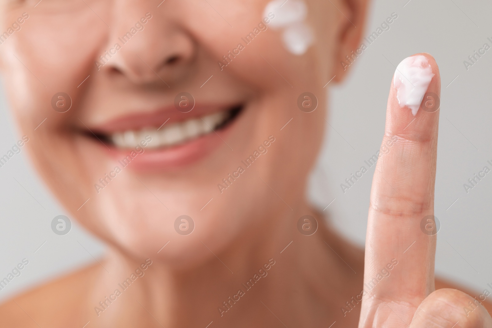 Photo of Senior woman with face cream on light background, closeup