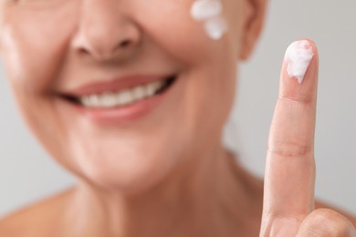 Senior woman with face cream on light background, closeup