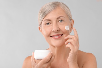 Senior woman with face cream on light background