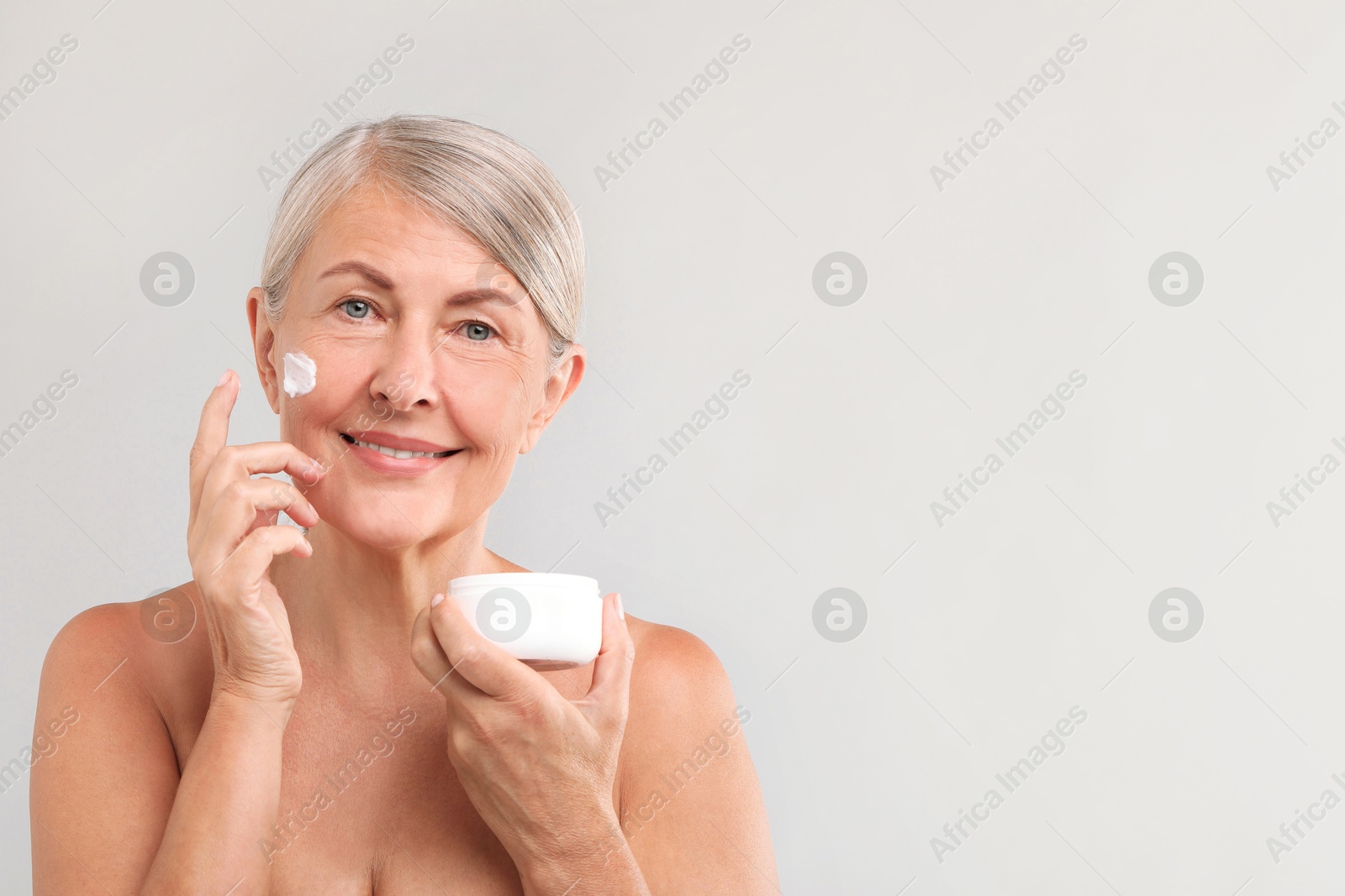 Photo of Senior woman with face cream on light background. Space for text