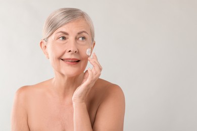 Senior woman applying face cream on light background. Space for text