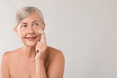 Photo of Senior woman applying face cream on light background. Space for text