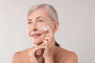 Photo of Senior woman applying face cream on light background