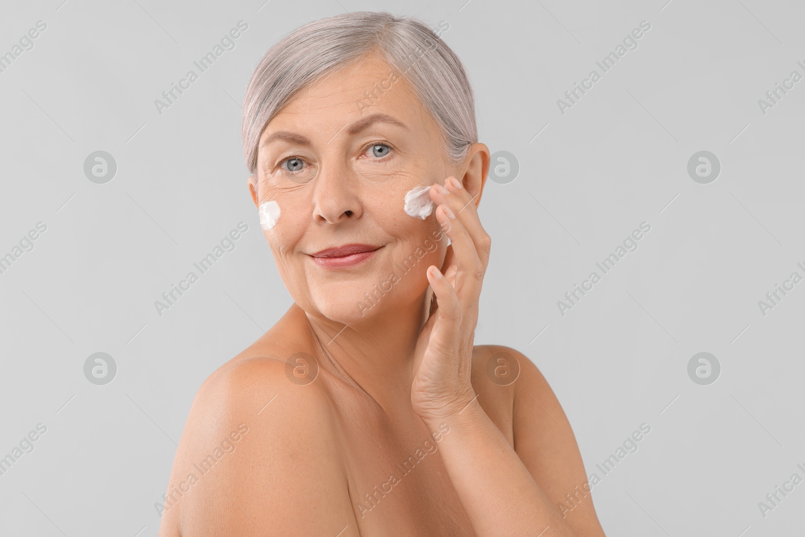 Photo of Senior woman applying face cream on light background