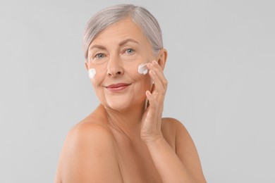 Photo of Senior woman applying face cream on light background