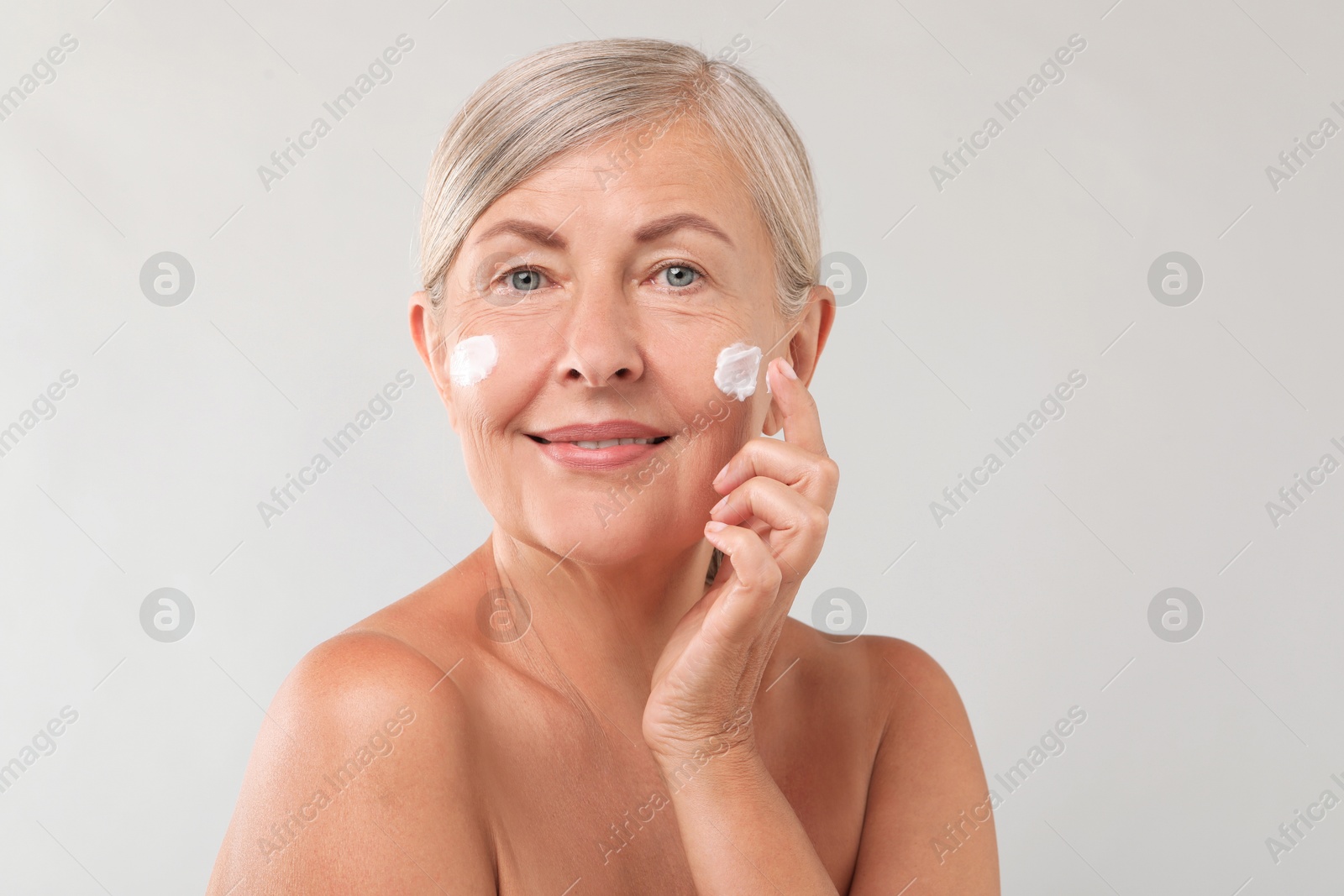 Photo of Senior woman applying face cream on light background