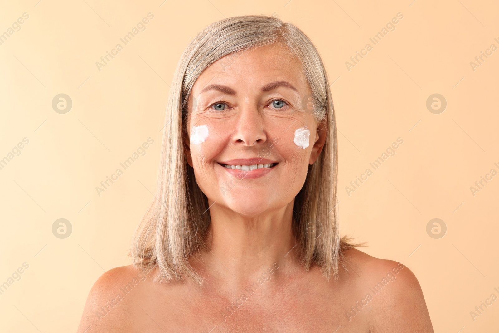 Photo of Senior woman with face cream on beige background