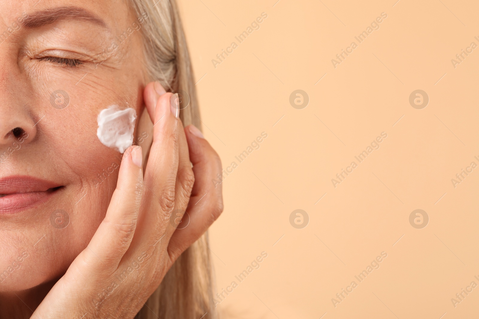 Photo of Senior woman with face cream on beige background, closeup. Space for text