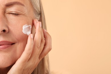 Senior woman with face cream on beige background, closeup. Space for text