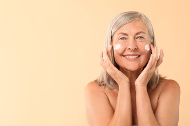 Senior woman with face cream on beige background. Space for text