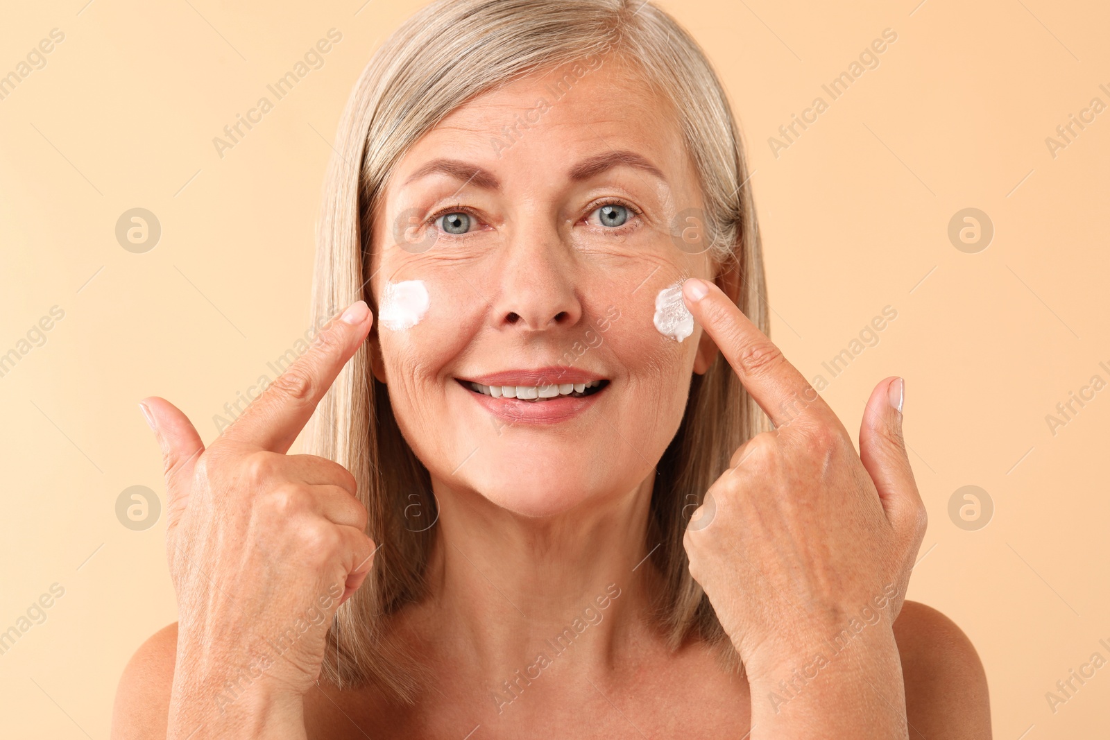 Photo of Senior woman with face cream on beige background