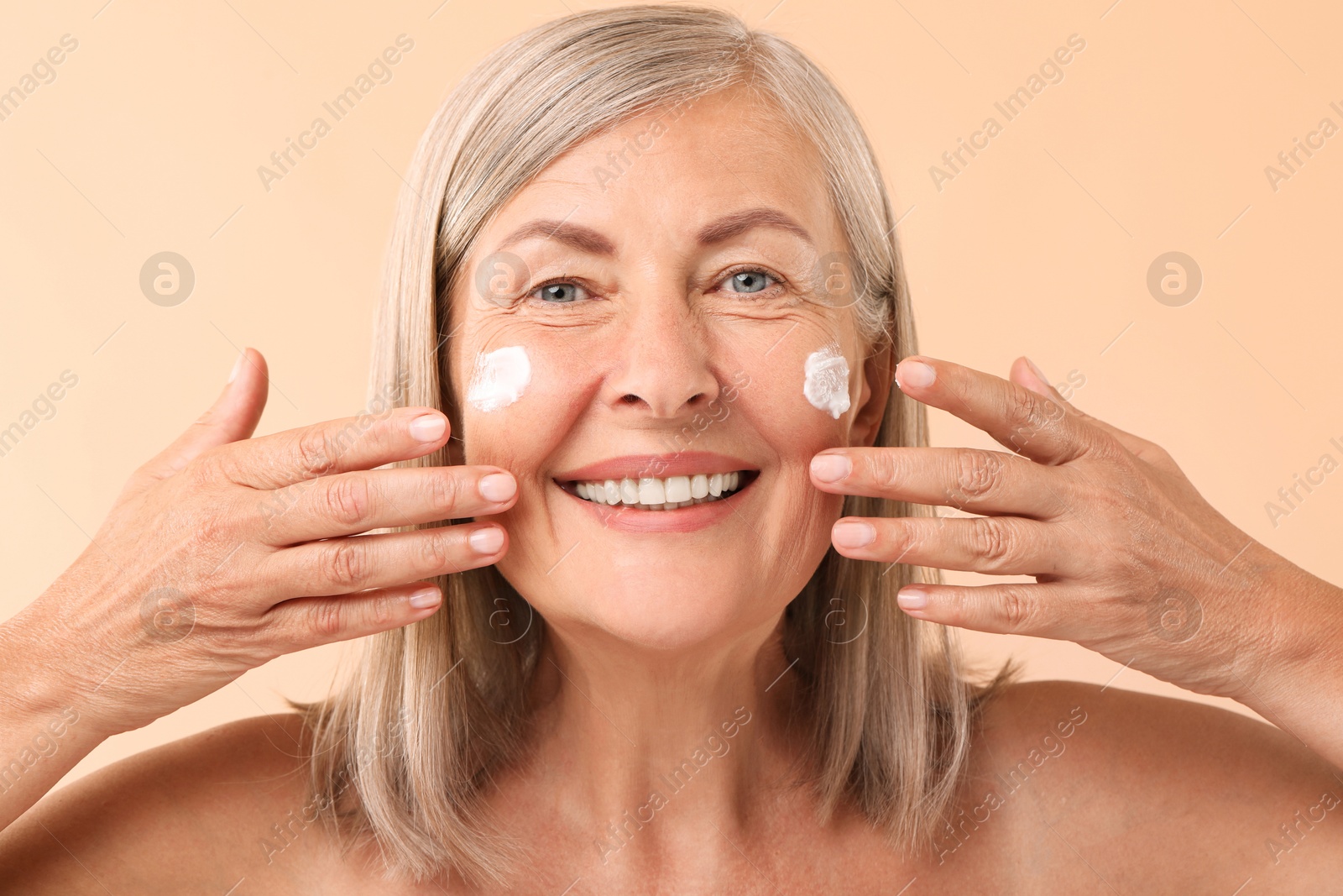 Photo of Senior woman with face cream on beige background