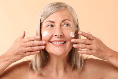 Senior woman with face cream on beige background