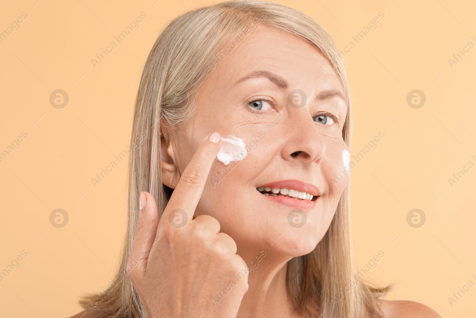 Photo of Senior woman applying face cream on beige background