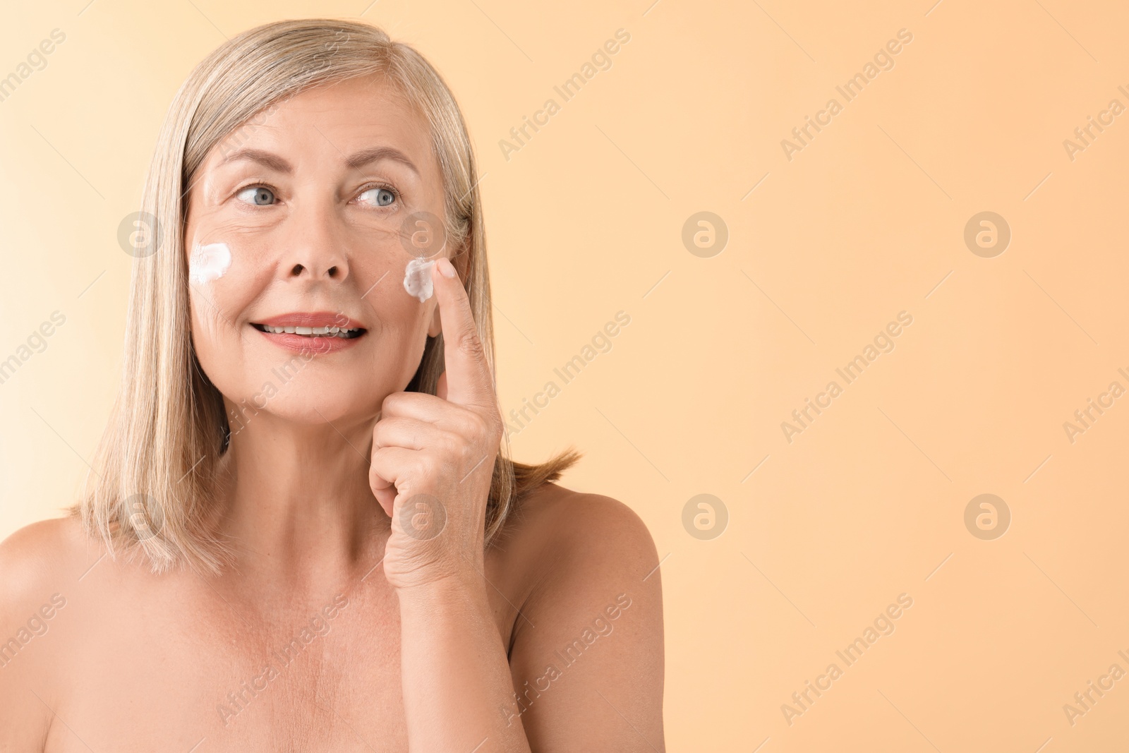 Photo of Senior woman applying face cream on beige background. Space for text