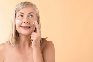 Senior woman applying face cream on beige background. Space for text