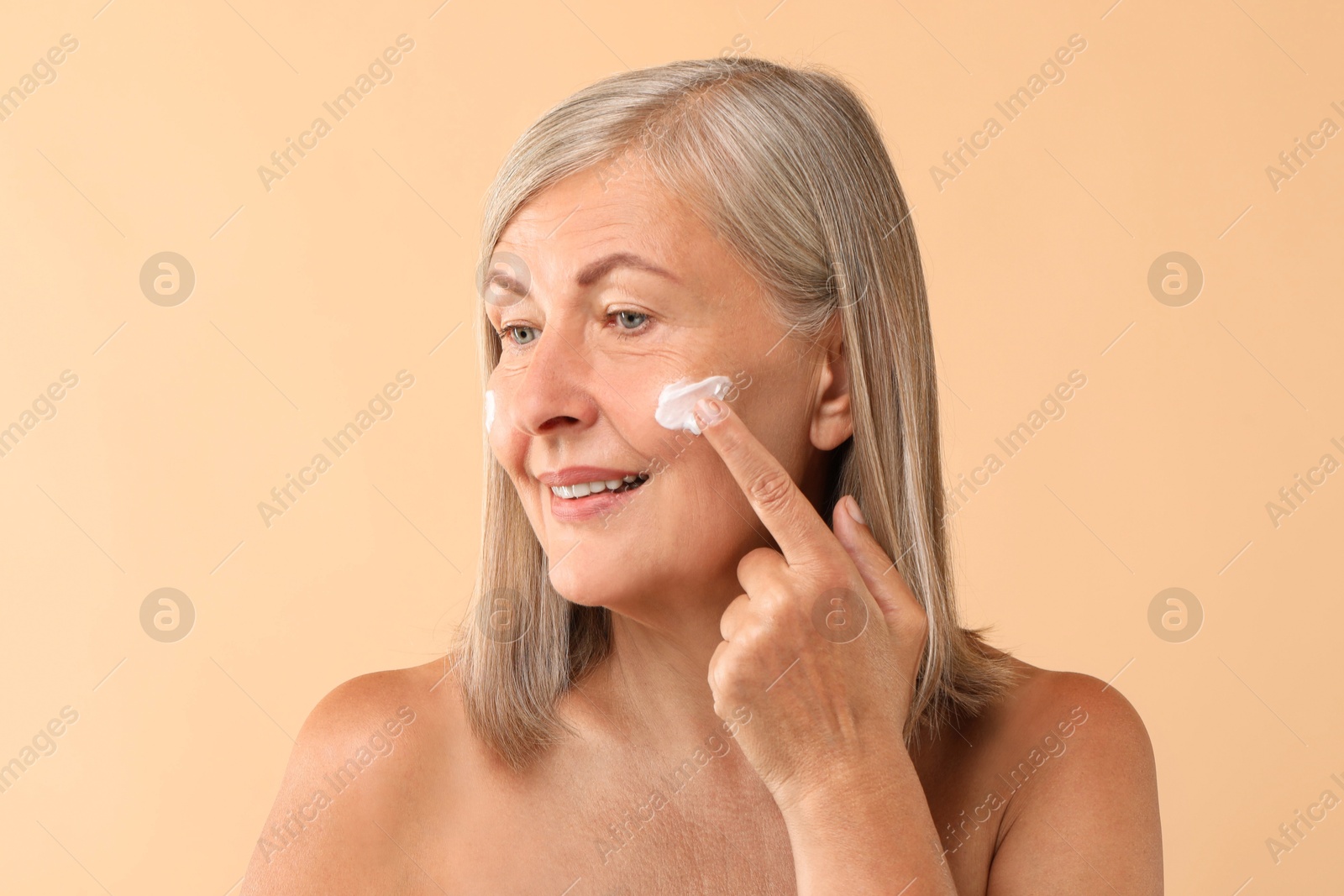 Photo of Senior woman applying face cream on beige background