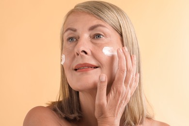 Photo of Senior woman applying face cream on beige background