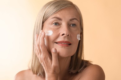 Photo of Senior woman applying face cream on beige background