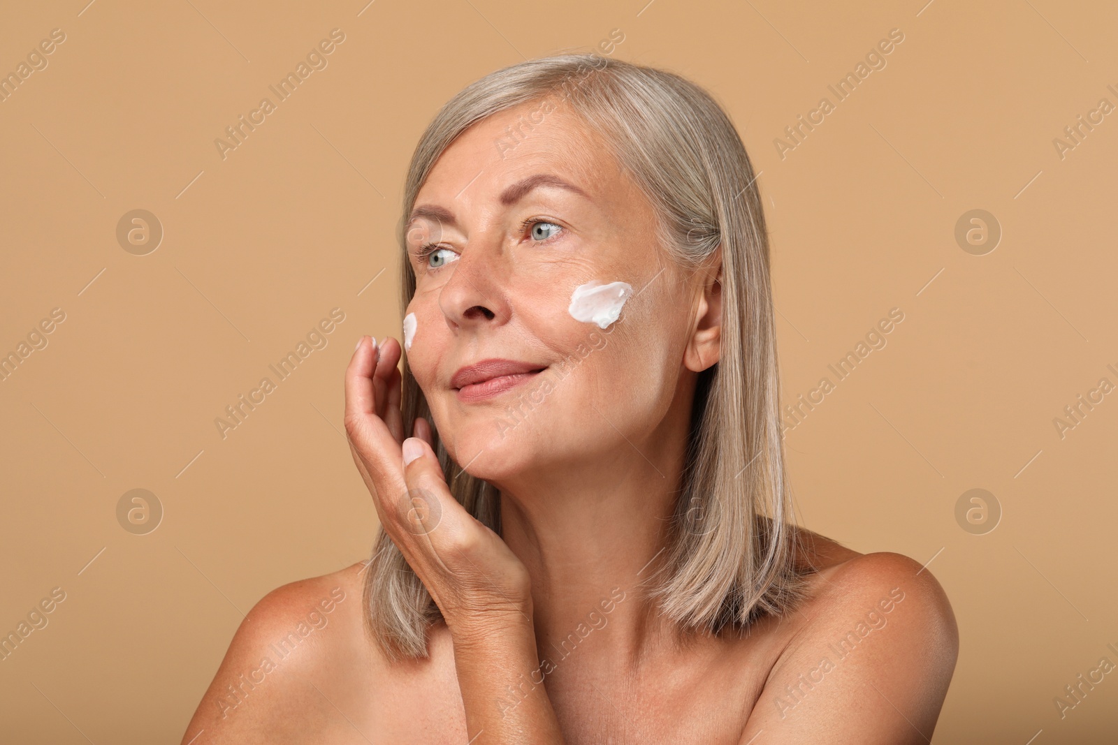 Photo of Senior woman applying face cream on beige background