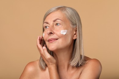 Photo of Senior woman applying face cream on beige background