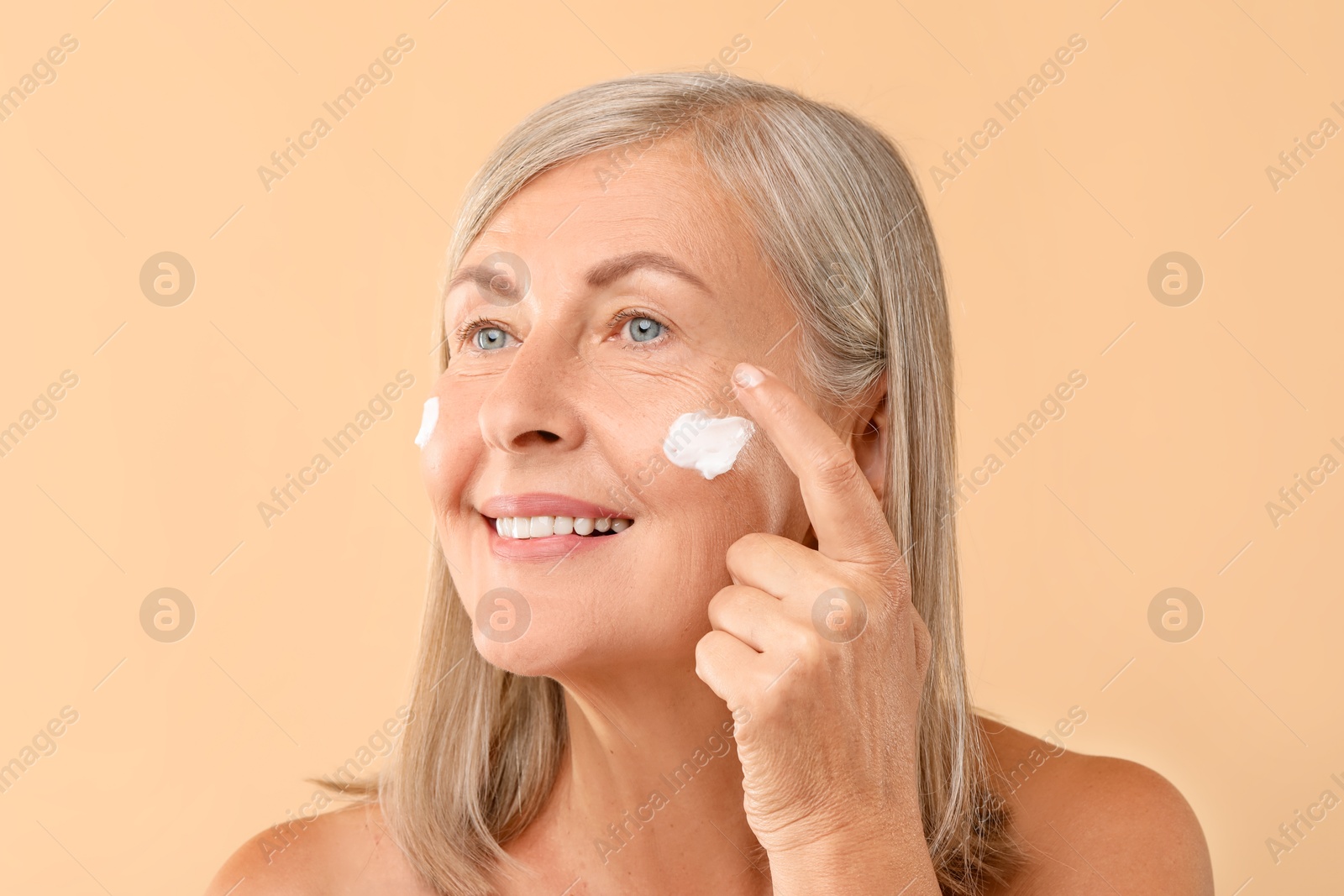 Photo of Senior woman applying face cream on beige background