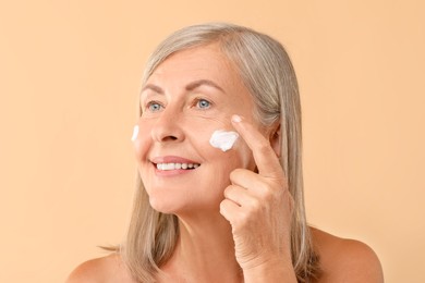 Senior woman applying face cream on beige background