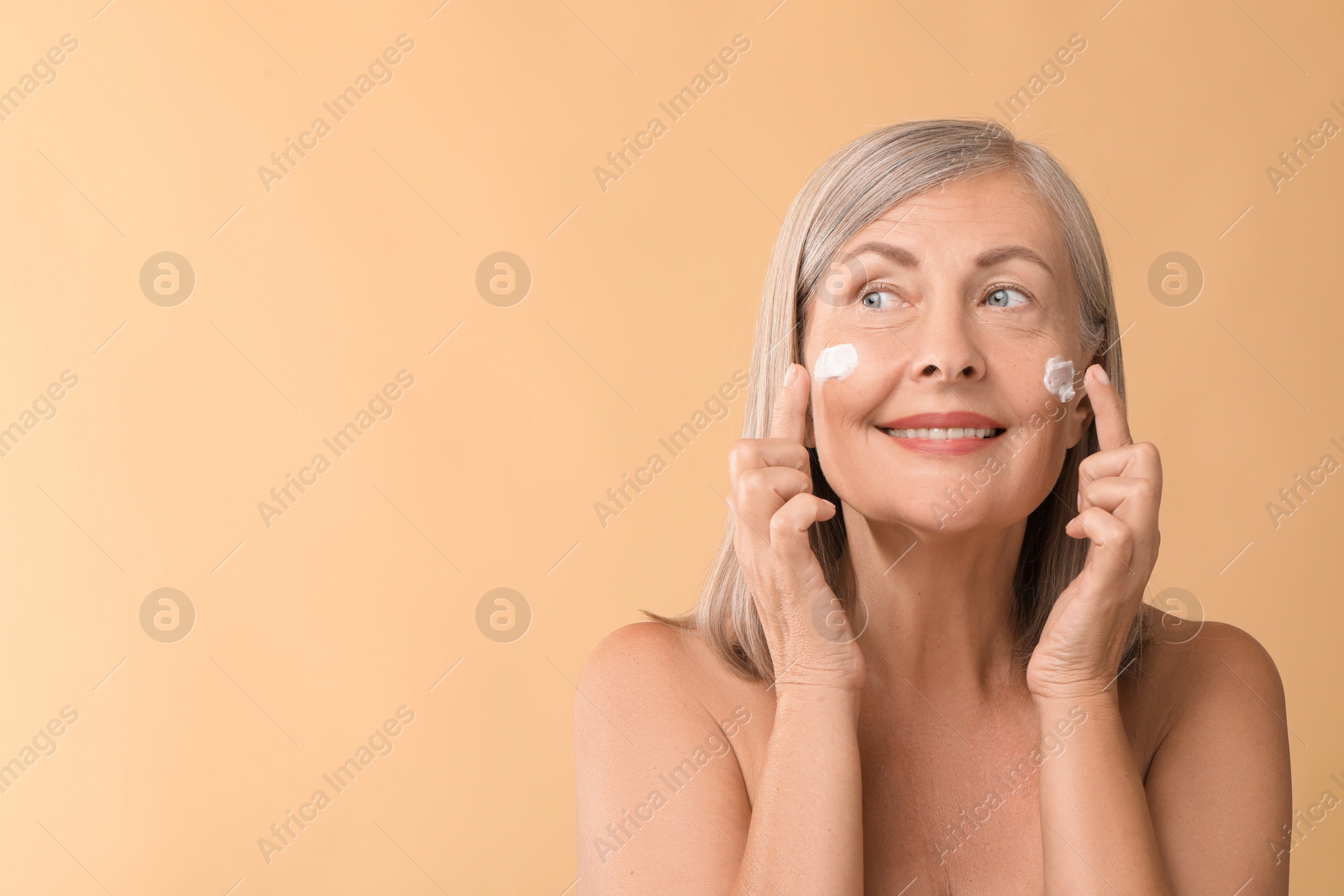 Photo of Senior woman with face cream on beige background. Space for text