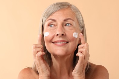 Senior woman with face cream on beige background