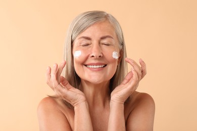 Senior woman with face cream on beige background