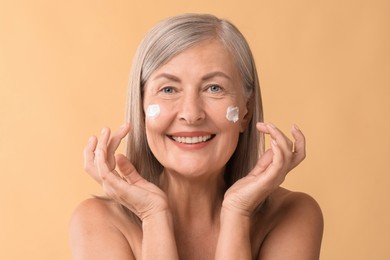 Senior woman with face cream on beige background