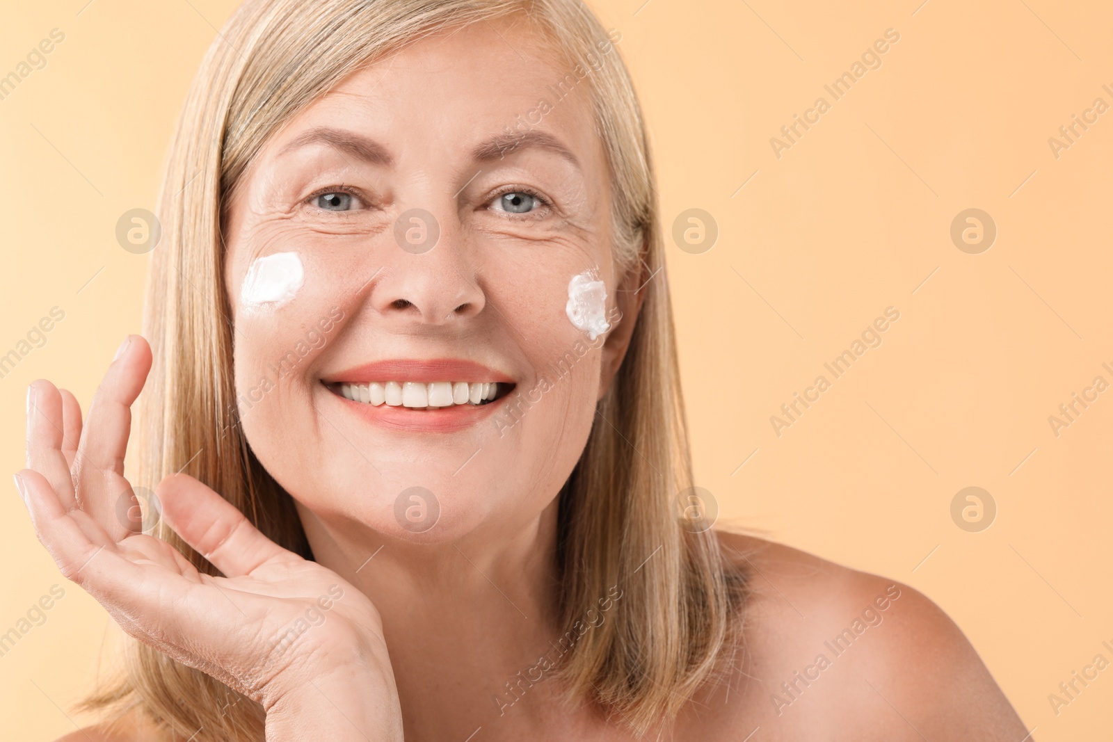 Photo of Senior woman with face cream on beige background, closeup