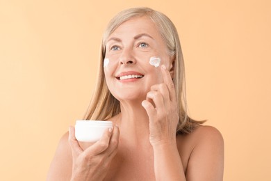 Photo of Senior woman applying face cream on beige background