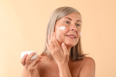 Photo of Senior woman applying face cream on beige background