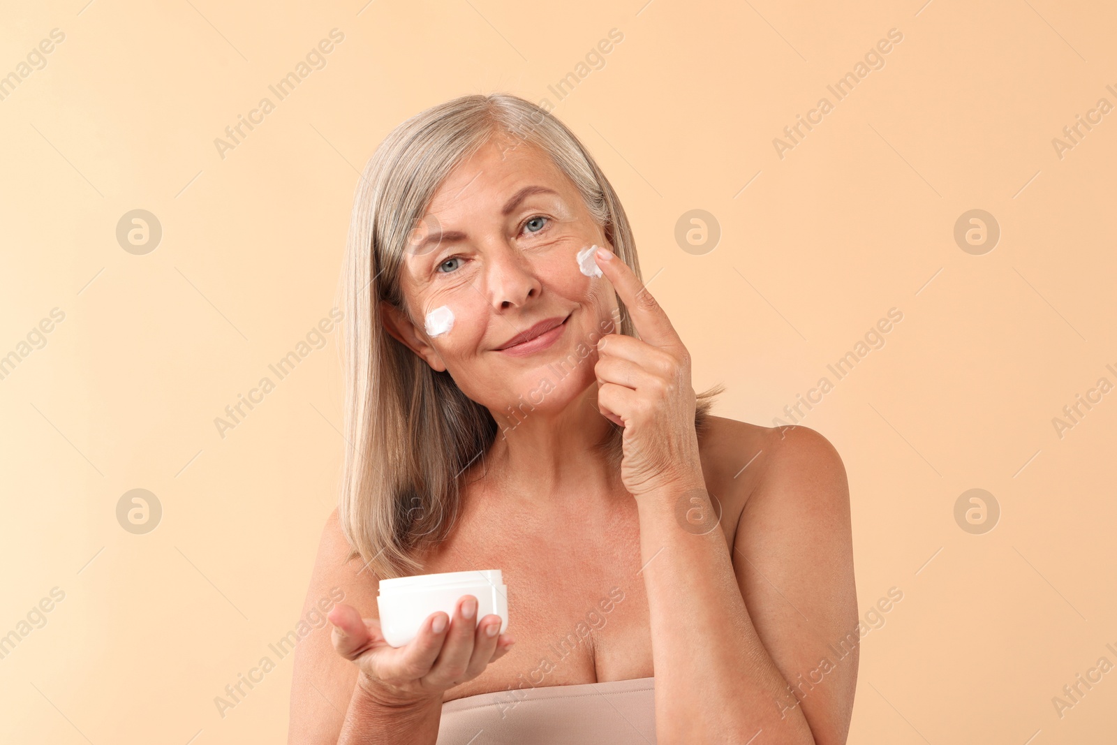 Photo of Senior woman applying face cream on beige background