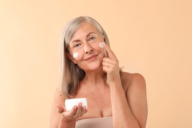 Senior woman applying face cream on beige background