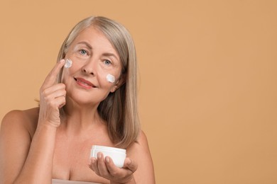 Photo of Senior woman applying face cream on beige background. Space for text