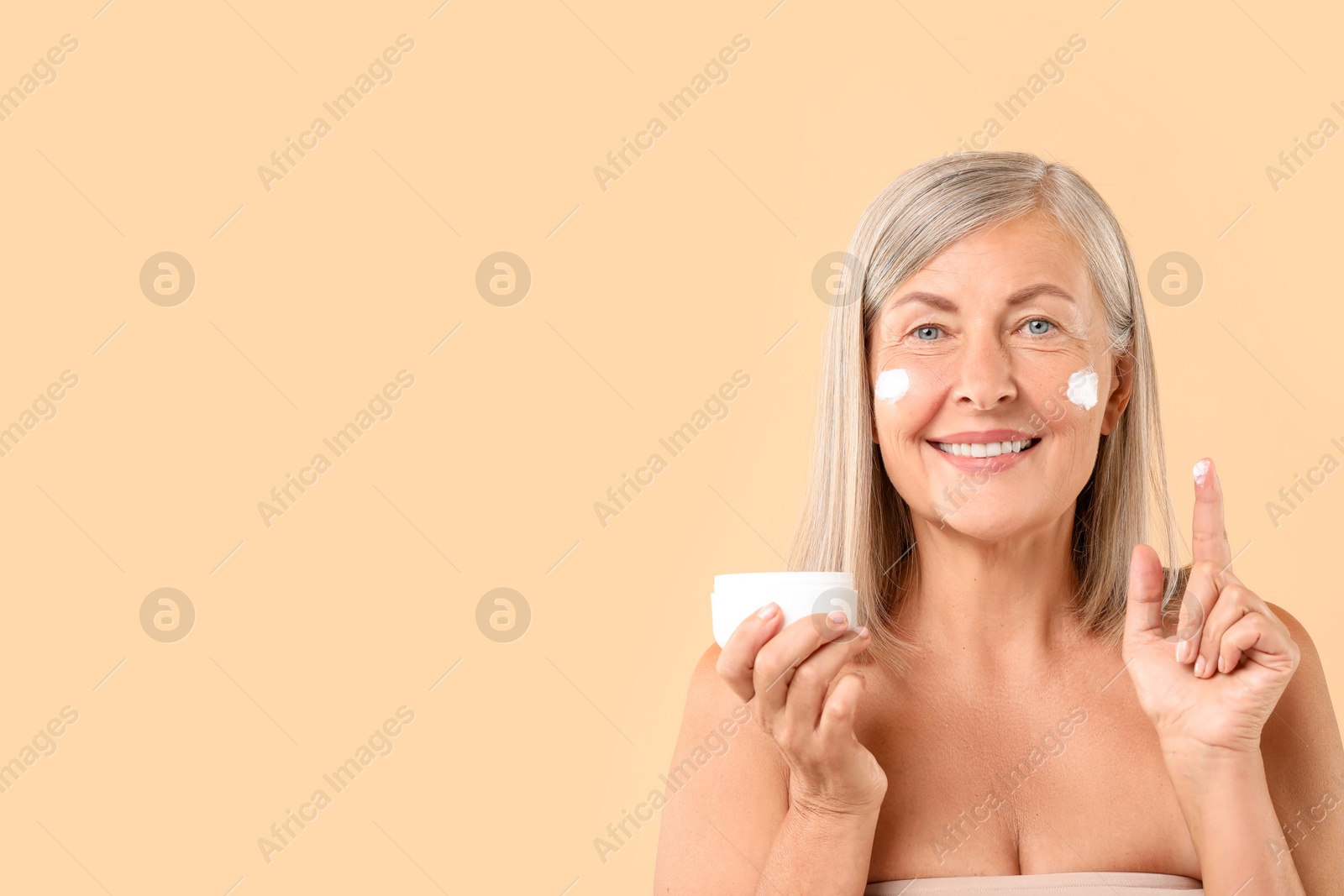 Photo of Senior woman with face cream on beige background. Space for text