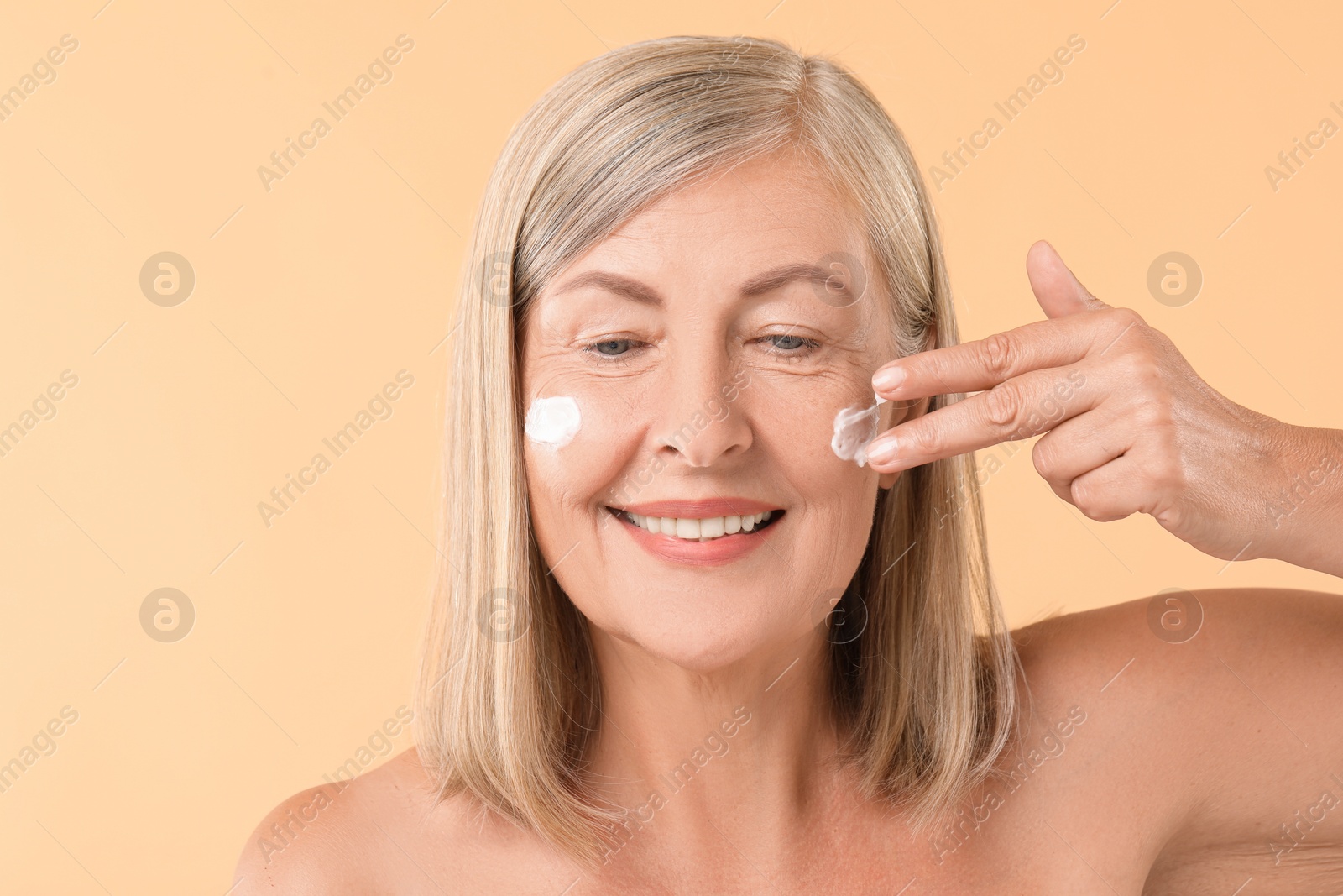 Photo of Senior woman applying face cream on beige background