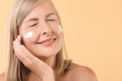 Senior woman with face cream on beige background, closeup. Space for text