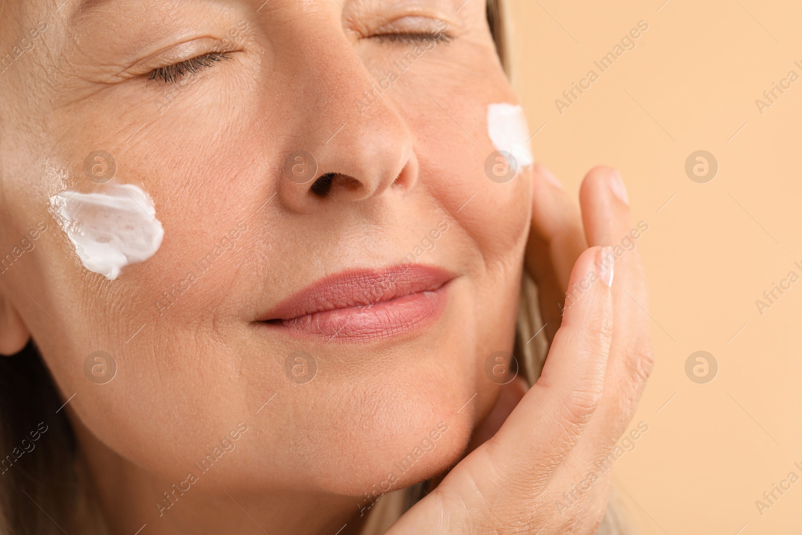 Photo of Senior woman with face cream on beige background, closeup