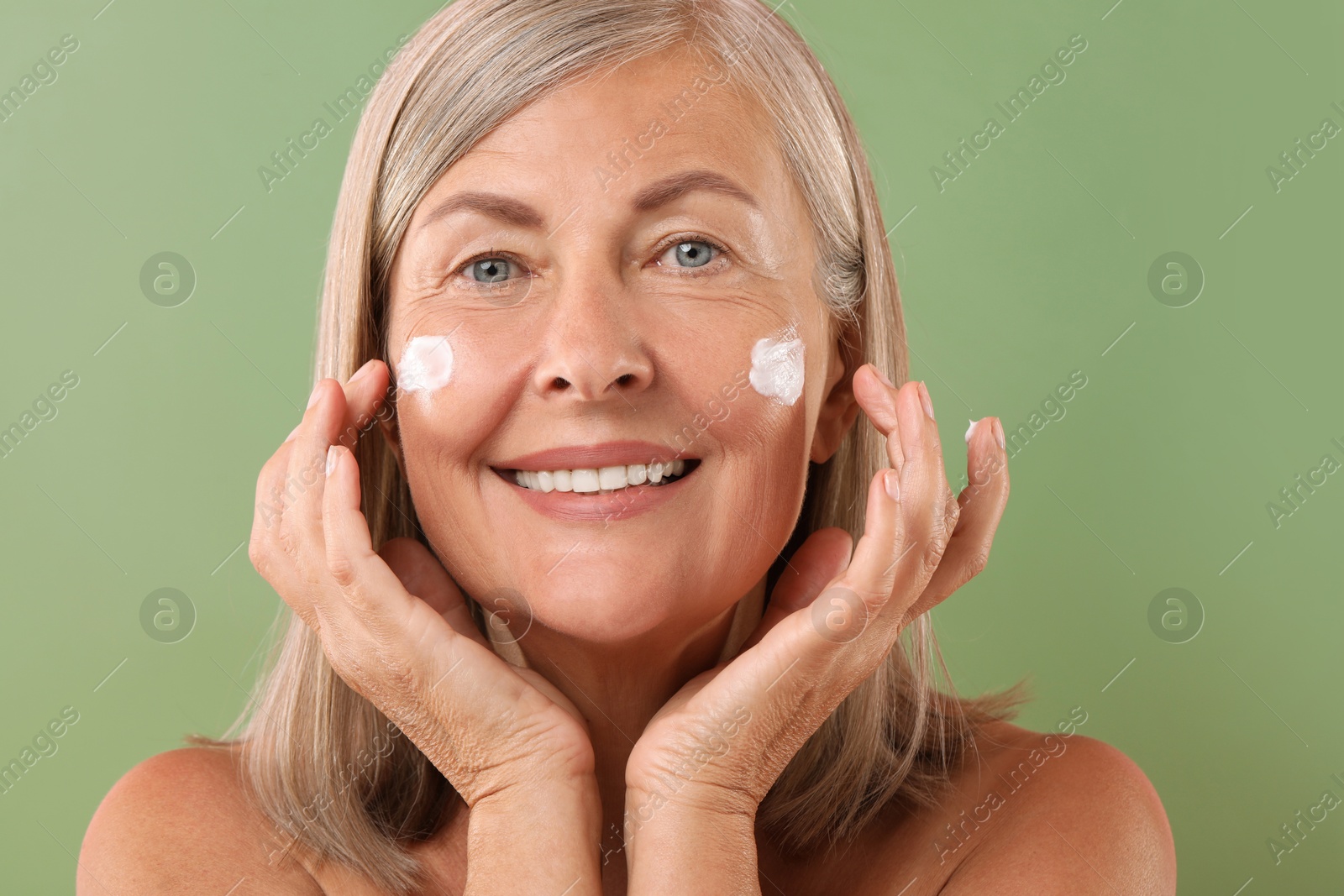 Photo of Senior woman with face cream on green background