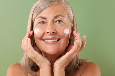 Senior woman with face cream on green background